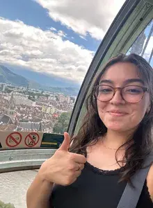 Natalia leaning towards a window with her thumb up, smiling