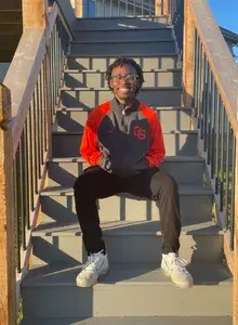 Nate sitting on stairs, smiling, with his hands in his pockets