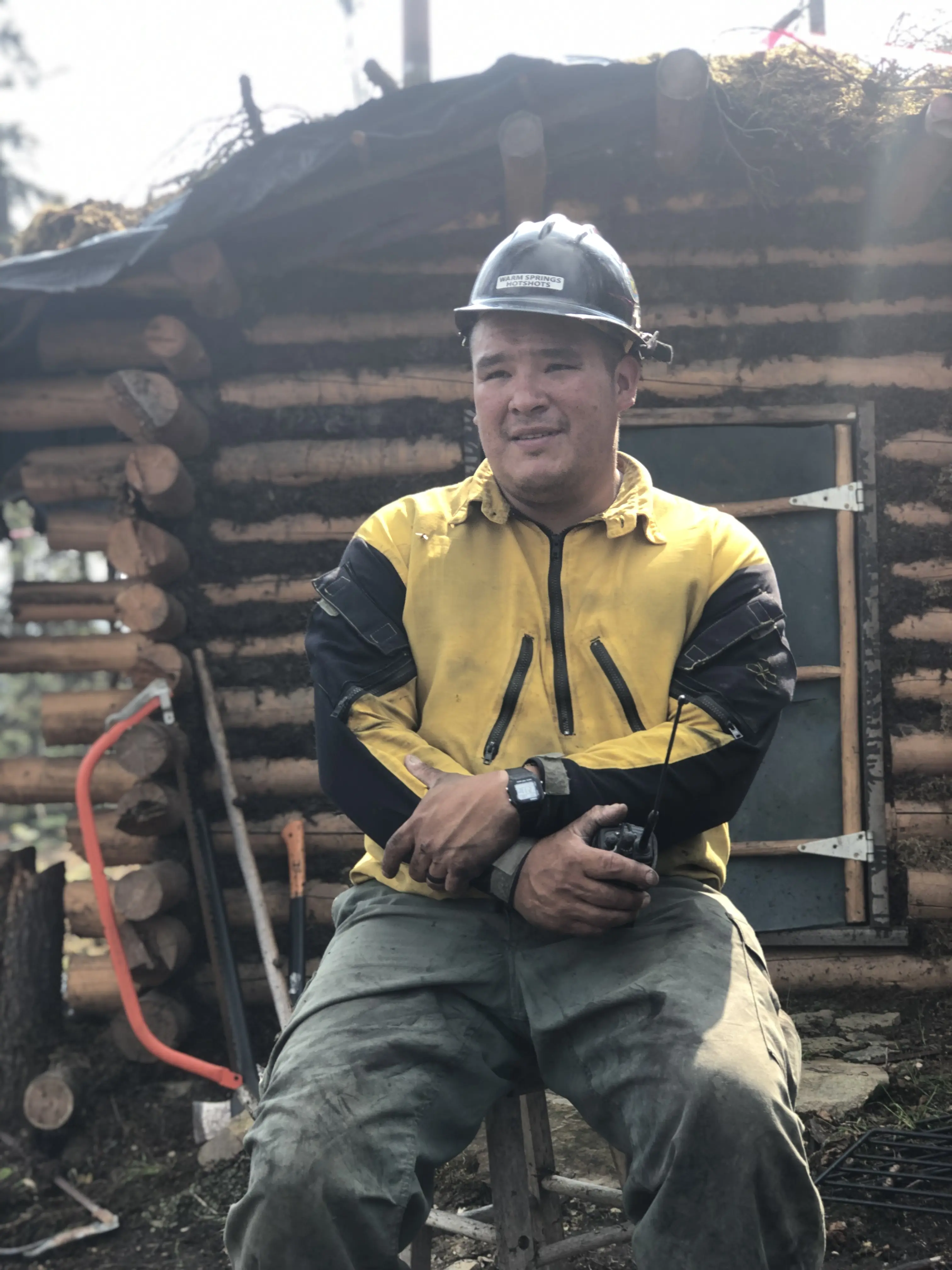 Glenn Jones in front of a wooden log house in work helmet and pants
